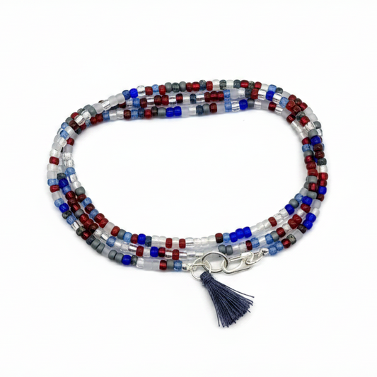 Beaded bracelet with shades of red, white & blue glass beads with a silver-plated clasp on a white background.