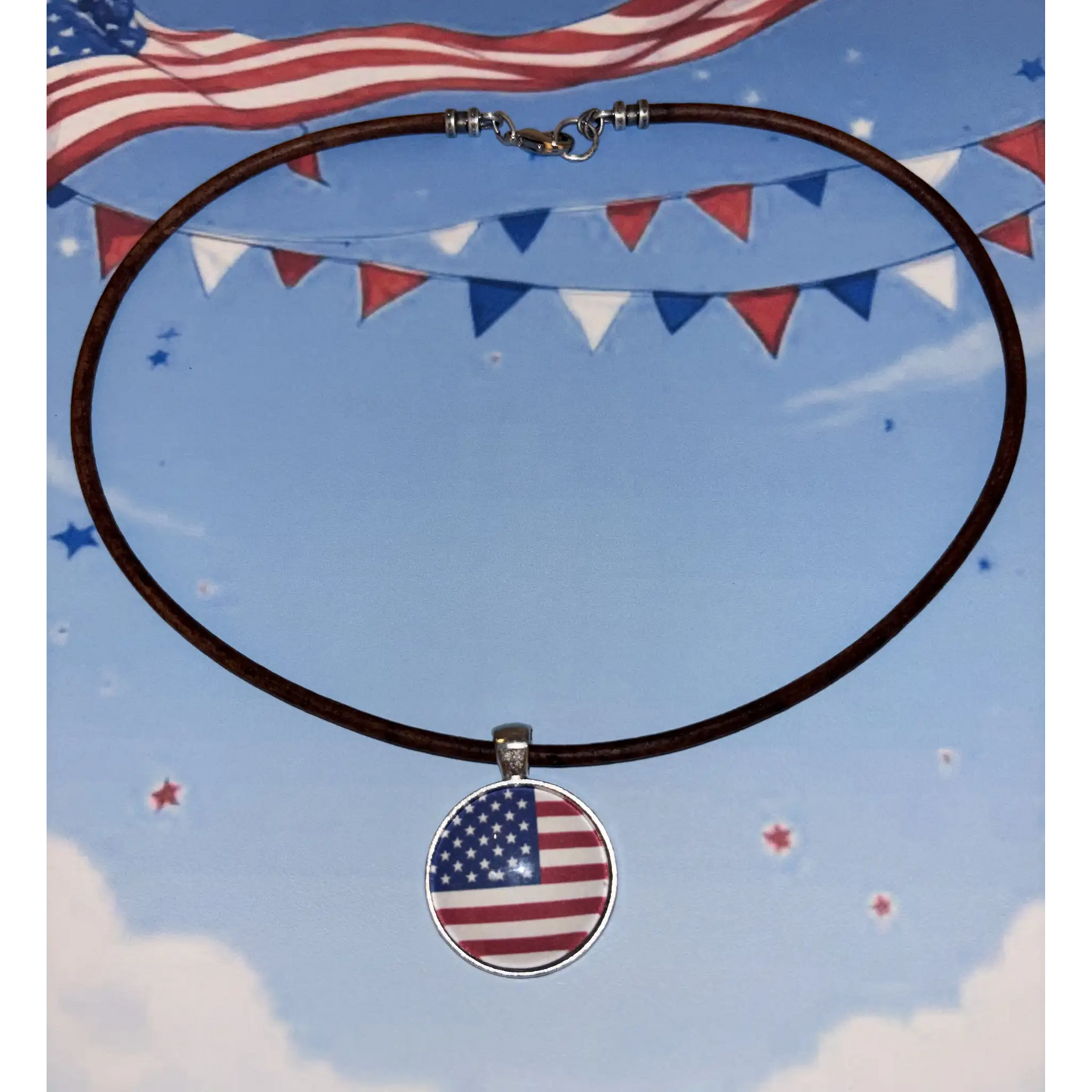 A circular pendant necklace featuring an American flag design, suspended on a dark brown leather cord with a silver-toned clasp, set against a patriotic blue sky background with bunting and stars.