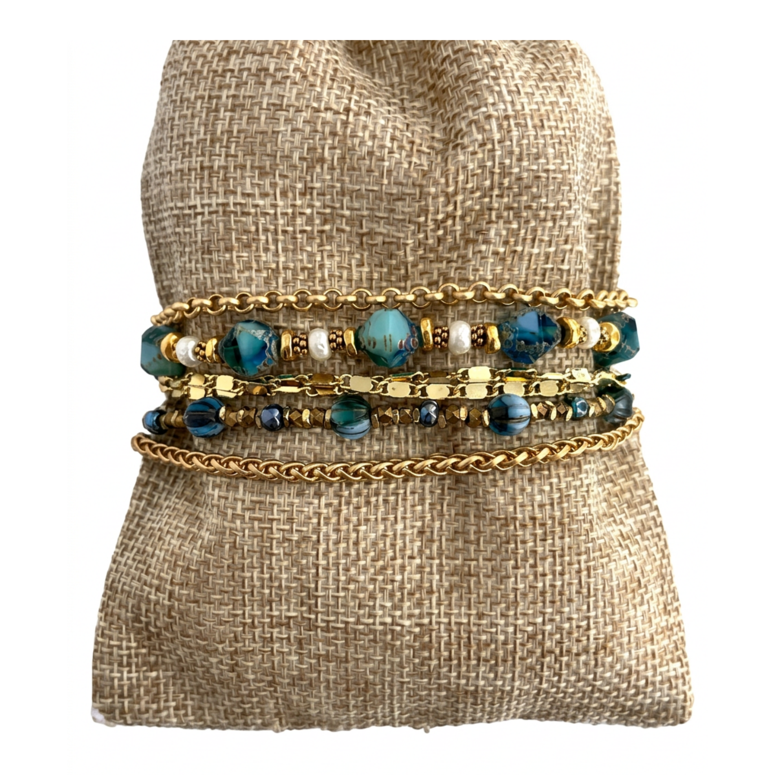 Back view of the aquamarine bead and gold chain wrap bracelet on a woven fabric pillow, highlighting the three distinct styles of gold-plated chain.