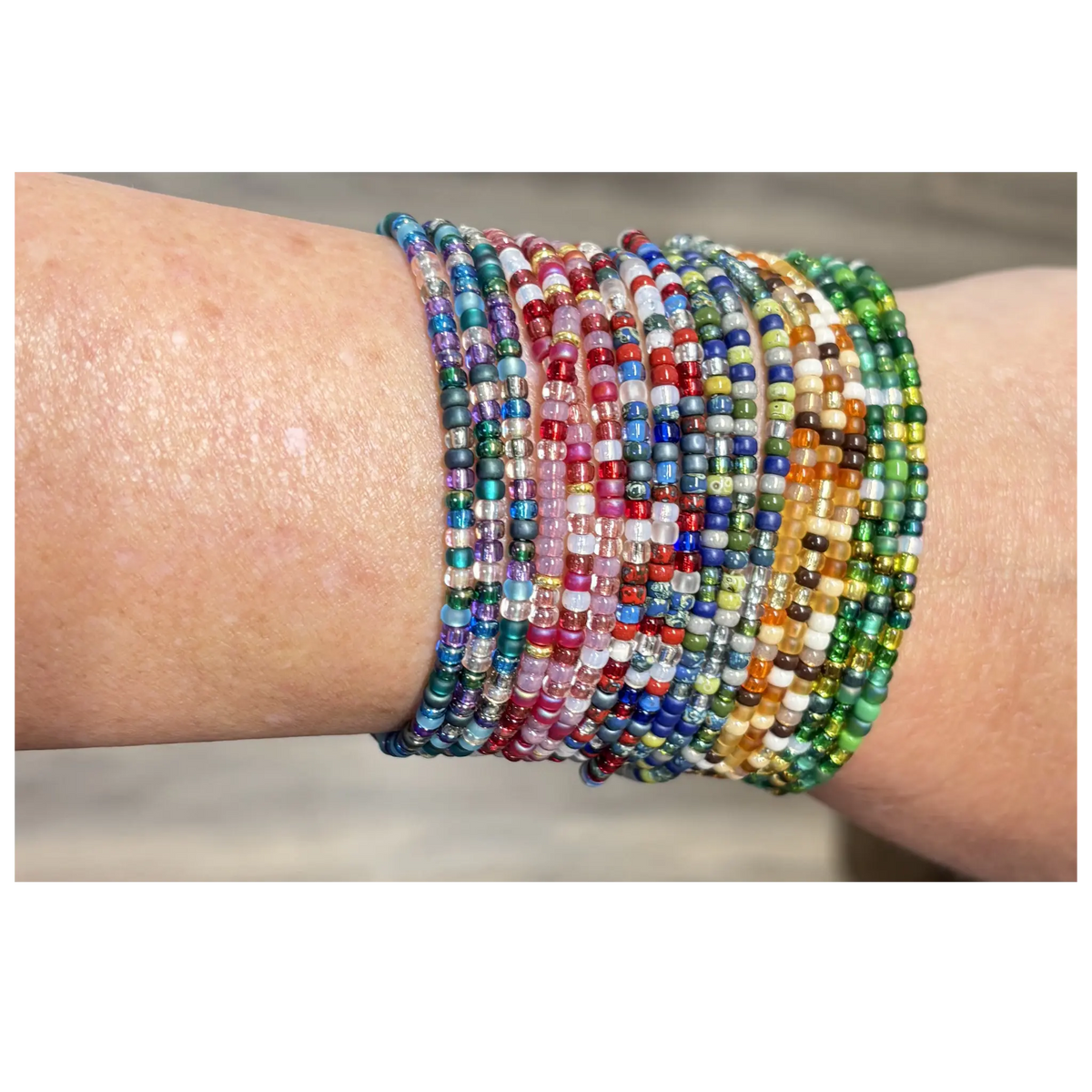 A close-up of a person's wrist wearing a stack of multiple beaded stretch bracelets in a rainbow of colors.