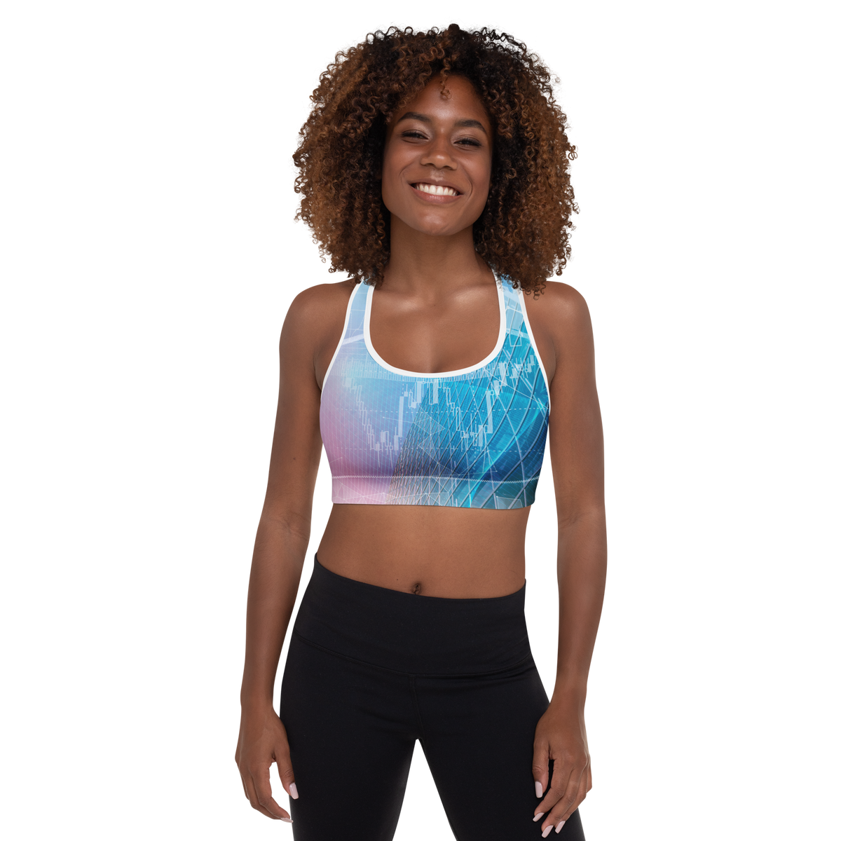 A woman with curly brown hair wearing a blue and purple abstract-patterned sports bra and black leggings, standing against a plain white background.