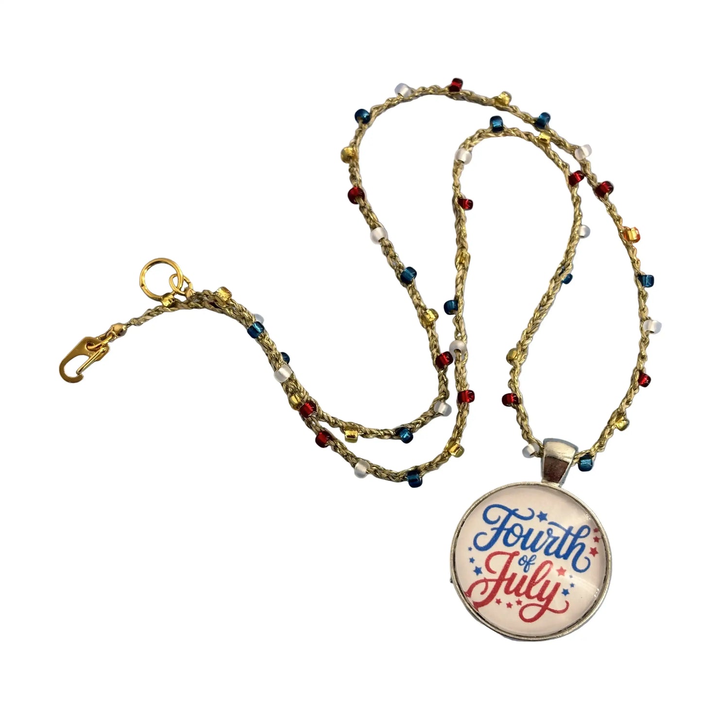 A beaded necklace with a round pendant that reads 'Fourth of July' in blue and red script on a white background, displayed on a patriotic blue surface with bunting.