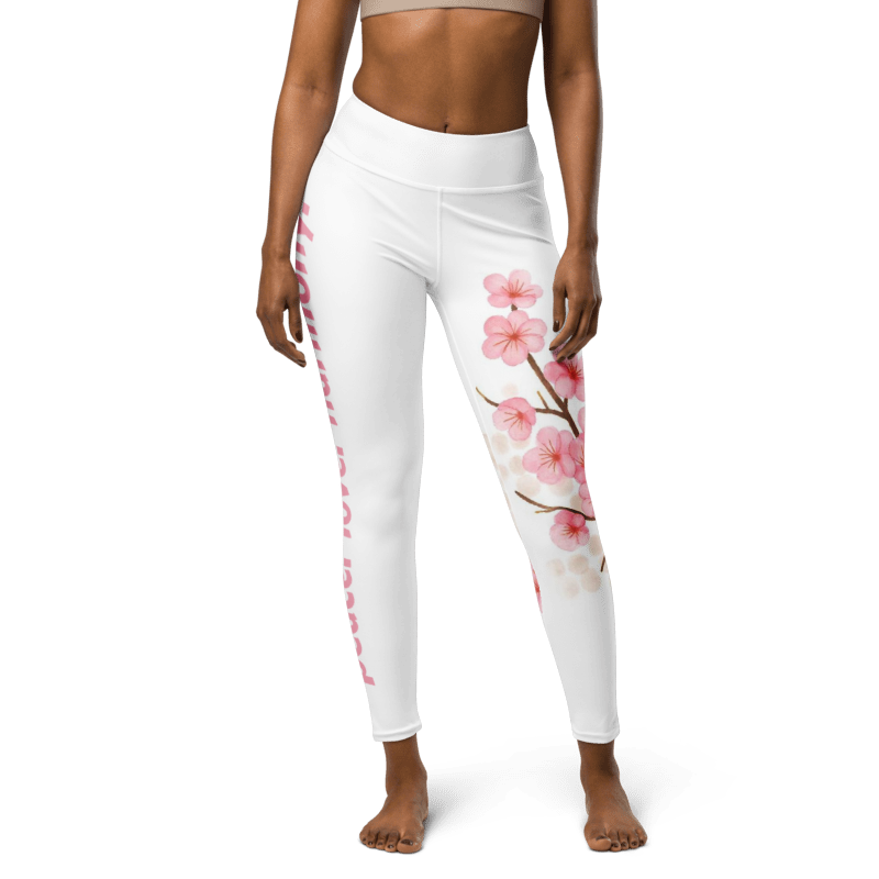 White high-waisted leggings with a pink cherry blossom branch print on the right leg and pink text running down the left leg, shown on a model against a white background.