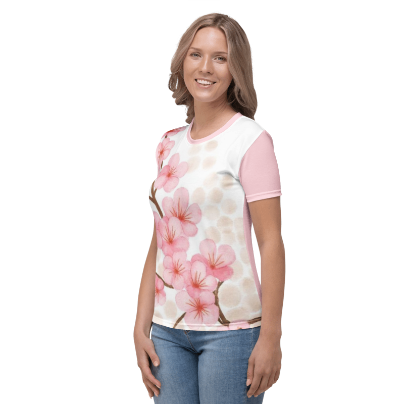 A smiling woman turned to her right, wearing the Sakura Soul regular-fit t-shirt featuring a watercolor cherry blossom branch graphic on a white background with pink sleeves.
