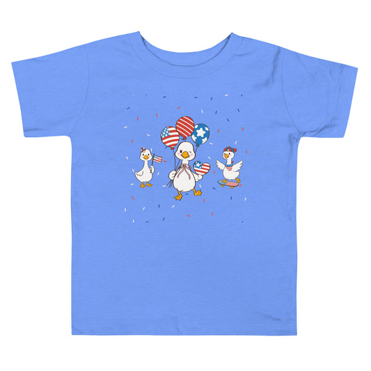 A patriotic toddler tee, featuring a playful print of festive ducks, balloons, and confetti on a white background.